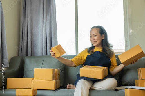 Successful old businesswoman smiling happily receiving new buzzer Asian woman owns a small business online with shipping boxes. concept of working at home © ArLawKa