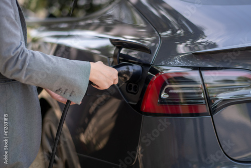 Progressive woman install cable plug to her electric car with charging station. Concept of the use of electric vehicles in a progressive lifestyle contributes to clean environment.