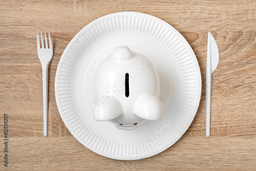 Piggy bank on the disposable plate with fork and knife, savings consumer concept