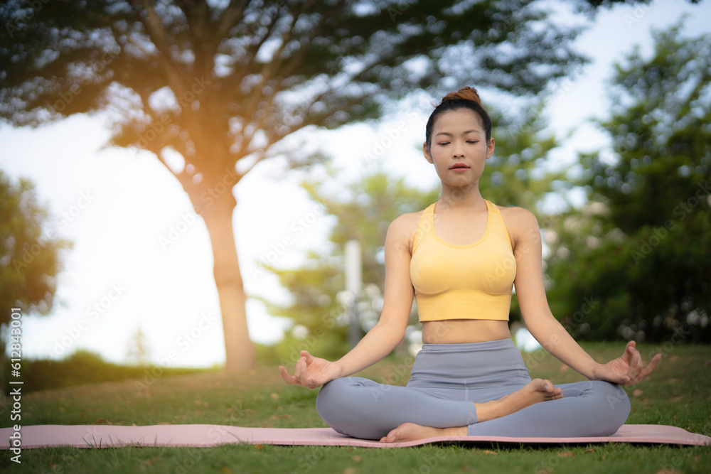 An asian woman do meditation on yoga mat at backyard or park, her eyes looking down, peaceful emotion. Healing mind and health concept in peaceful place.