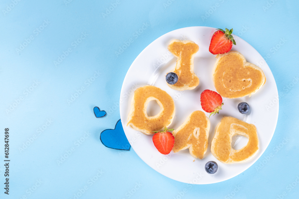 Father's day holiday idea for a cute surprise gift. Child preparing breakfast for dad, creatively decorated pancakes with the inscription I love Dad. Top view copy space, blue background Father's day holiday idea for a cute surprise gift. Child preparing breakfast for dad, creatively decorated pancakes with the inscription I love Dad. Top view copy space, blue background