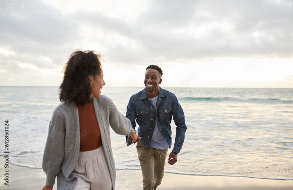 Smiling young multiethnic couple running hand in hand on a sandy beach Smiling young multiethnic couple running hand in hand on a sandy beach