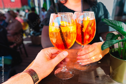 Couple celebratory toast with aperol spritz orange alcoholic cocktails at outdoors cocktail bar at night.Close up.