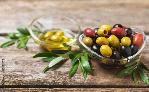 Green, black and red olives on a brown wooden background. Various types of olives in bowls and olive oil with fresh olive leaves. Copy space. Place for text. Mediterranean food. Vegan.