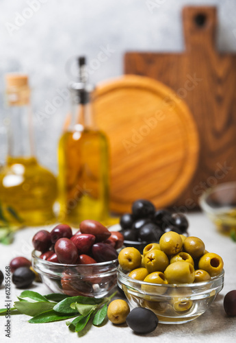 Green, black and red olives on a textured marble background. Various types of olives in bowls and olive oil with fresh olive leaves. Copy space. Place for text. Mediterranean food. Vegan.