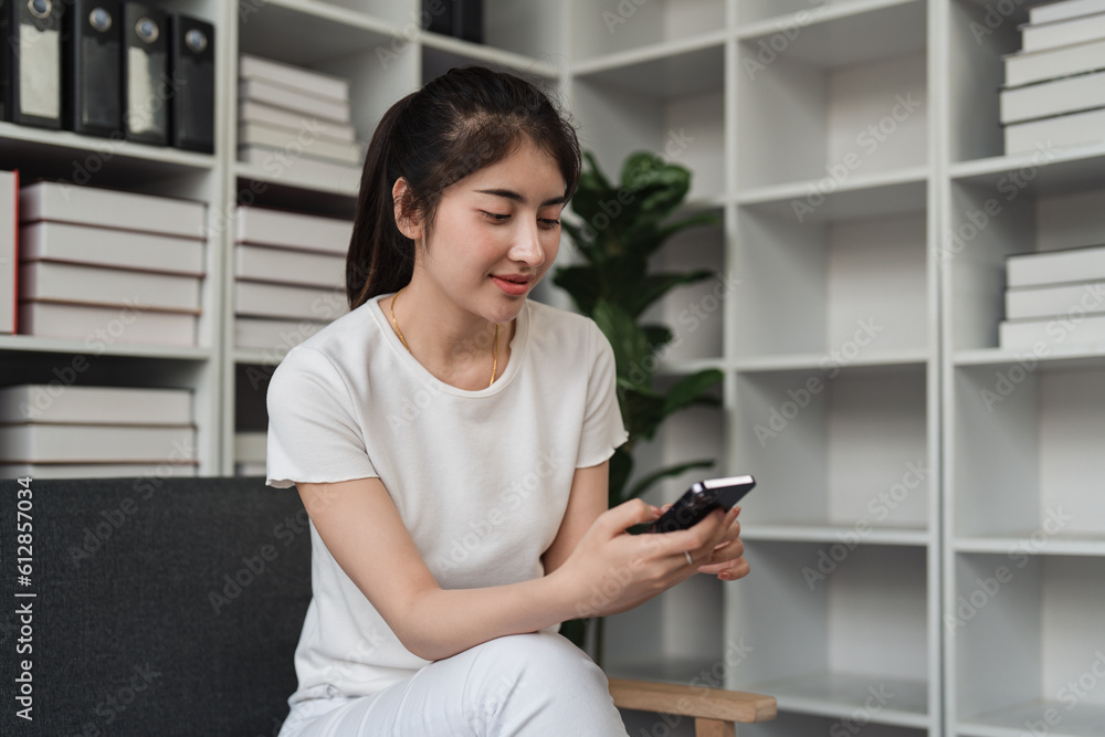 Young relaxed smiling pretty woman relaxing sitting on sofa at home. Female feeling joy enjoying with mobile phone on cozy couch