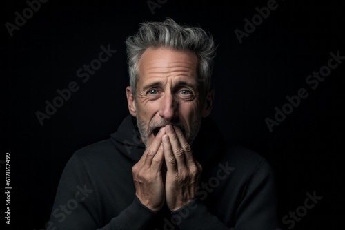 Headshot portrait photography of a satisfied mature man covering his mouth against a matte black background. With generative AI technology