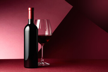 Bottle and glass of red wine on a red background.