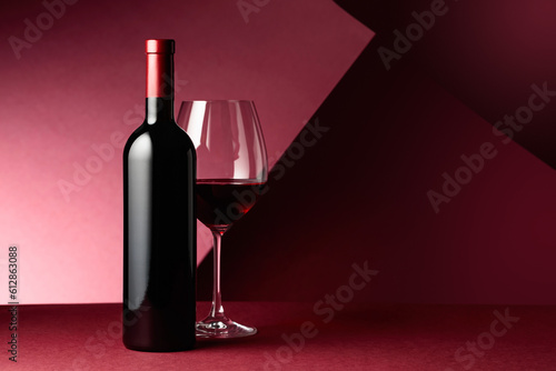 Bottle and glass of red wine on a red background.