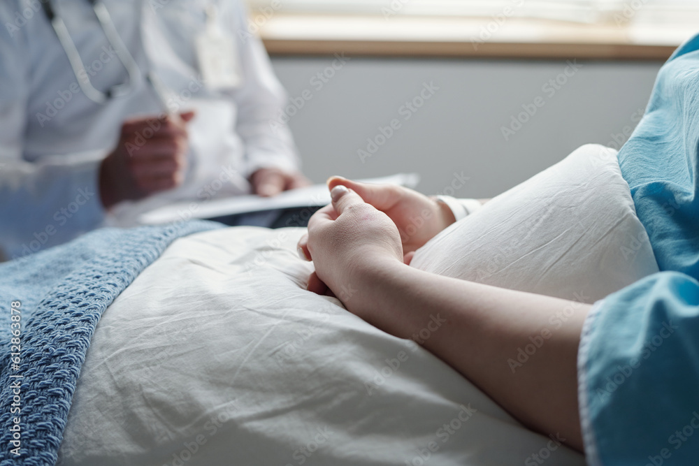 Close-up of hands of young woman with oncological disease sitting under blanket in bed and consulting with her doctor after medical treatment Close-up of hands of young woman with oncological disease sitting under blanket in bed and consulting with her doctor after medical treatment