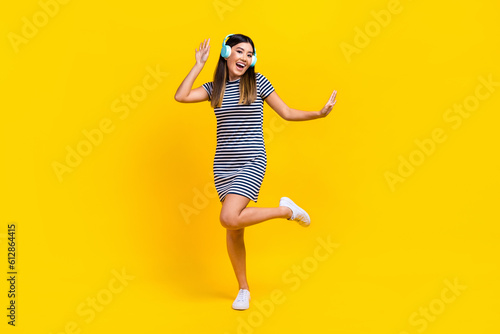 Full length photo of excited sweet woman dressed striped outfit headphones dancing having fun isolated yellow color background