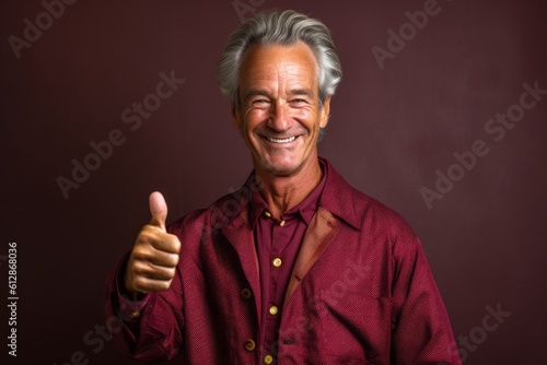 Lifestyle portrait photography of a joyful mature man showing a thumb up against a rich maroon background. With generative AI technology
