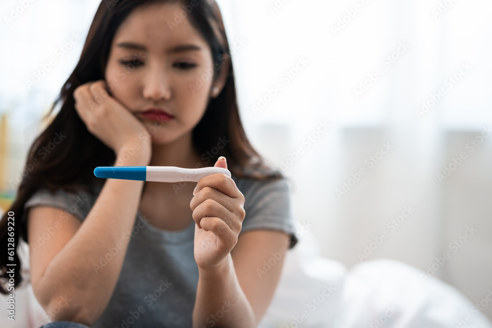 Asian woman sitting bed feeling disappointed when see the pregnancy test result. Woman feels worry and not ready to be a mother. Man feeling stress about the future kid holding head. Asian woman sitting bed feeling disappointed when see the pregnancy test result. Woman feels worry and not ready to be a mother. Man feeling stress about the future kid holding head.