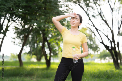 Asian woman wiping sweat and about to drink water after running in the park.