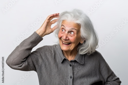 Headshot portrait photography of a grinning old woman scratching head in gesture of confusion against a pearl white background. With generative AI technology