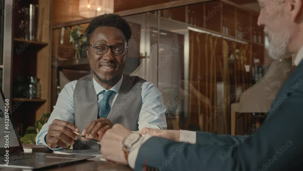 Waist up of two successful multiracial business partners discussing project ideas during meeting in expensive restaurant with bar Waist up of two successful multiracial business partners discussing project ideas during meeting in expensive restaurant with bar
