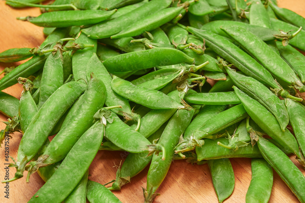 Fototapeta premium green ripe plucked pea pods on a wooden kitchen cutting board close-up