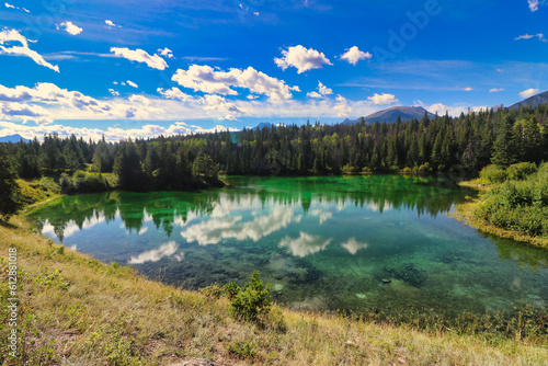Clouds scud across a bright blue sky and are reflected in the glassy waters of the lakes of the Valley of Five Lakes in the Jasper region of the Canada Rockies