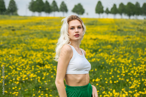 Young beautiful blonde woman posing in a spring field of dandelions