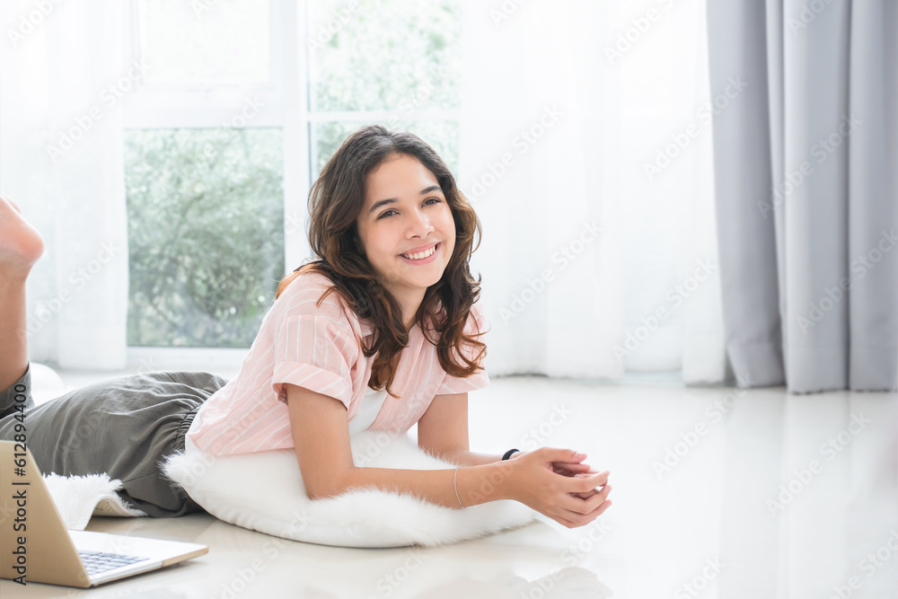 Portrait of Caucasian teenage girl in casual clothes smiling, lying on floor at home while using laptop Portrait of Caucasian teenage girl in casual clothes smiling, lying on floor at home while using laptop