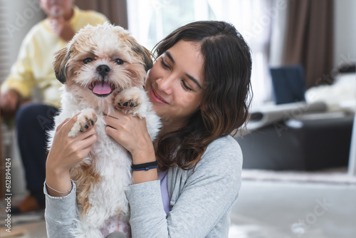 Portrait of Caucasian teenage girl playing with shih tzu puppy dog at home. Young beautiful woman sitting on floor, smiling, having fun holding little fluffy dog pet with love and care