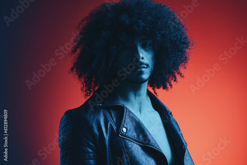 Portrait of fashion man with curly hair on red background multinational, colored light, black leather jacket trend, modern concept.