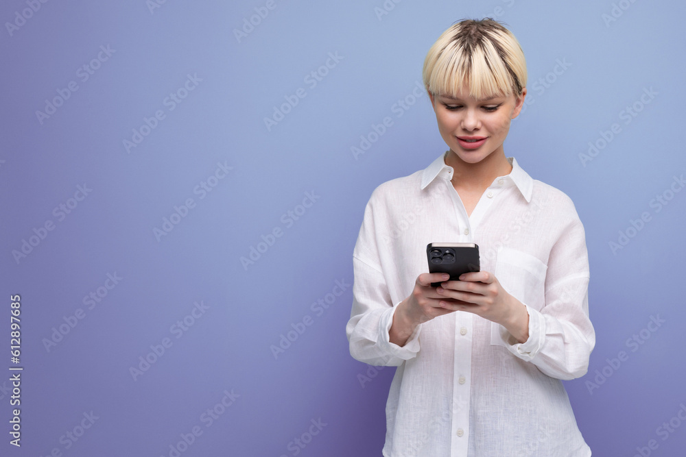 young pretty caucasian office worker woman with short blond hair dressed in a white blouse uses a smartphone on the background with copy space. business concept young pretty caucasian office worker woman with short blond hair dressed in a white blouse uses a smartphone on the background with copy space. business concept