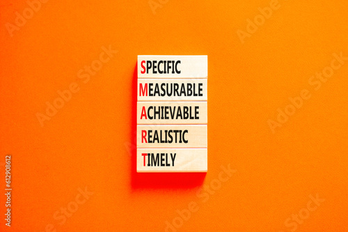SMART symbol. Concept words SMART specific measurable achievable realistic timely on wooden block. Beautiful orange background. Business SMART specific measurable achievable realistic timely concept.