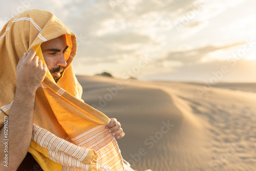 man in the desert on expedition with his face covered against the light at sunset looking at the camera, in the golden light, traveling the world