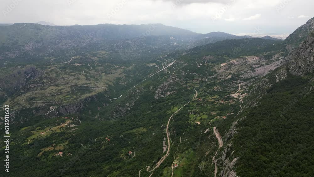 A green valley surrounded by beautiful mountains and a mountain road passing through the valley. Mountains in the clouds. Durmitor National Park. Montenegro. Aerial view. A green valley surrounded by beautiful mountains and a mountain road passing through the valley. Mountains in the clouds. Durmitor National Park. Montenegro. Aerial view.
