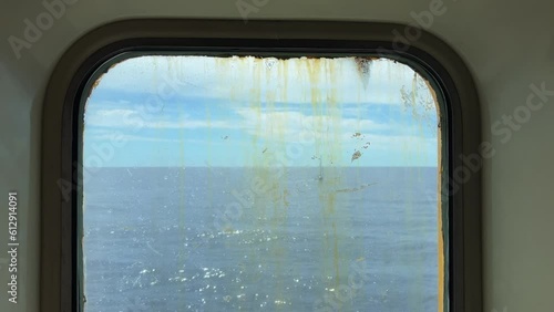 Sailboat sailing on calm sea water as seen through dirty and rusty window of navigating old ferry. Closeup passenger point of view photo