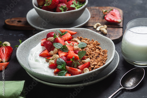 Granola with yogurt and strawberries in a plate on a dark background
