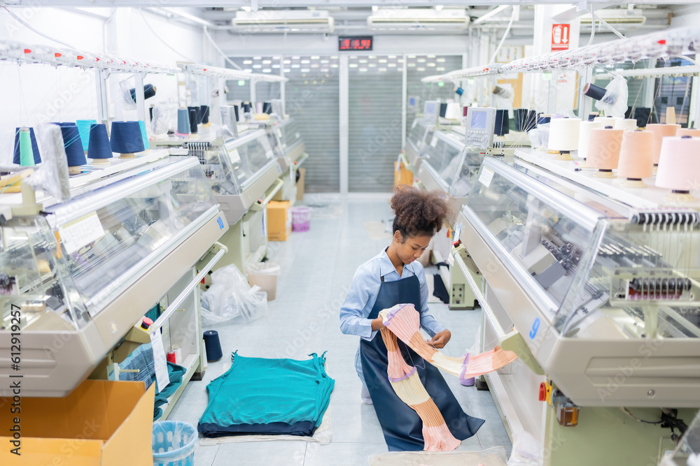 American female designer, weaver sitting in the middle of the room Checking and touching fabrics produced by weaving machines. There is a sewing machine working. in a large weaving industry