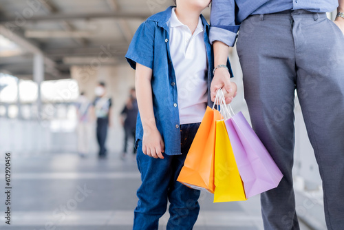 Crop Asian single father and son's hands holding shopping bags while walking to bus station corrior. After tire from shoping at shoping mall.