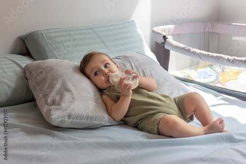 Bebé de ocho meses tomando su leche en su biberón en su cuarto en un día soleado.