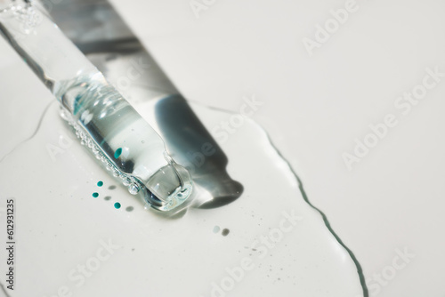 Pipette and drop of cosmetic product with blue particles, selective focus