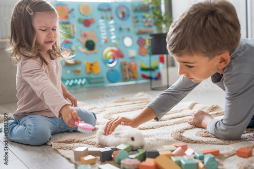 Two year old toddler girl and preschooler boy playing at home with white rabbit, early child development and unusuall bonding concept photo