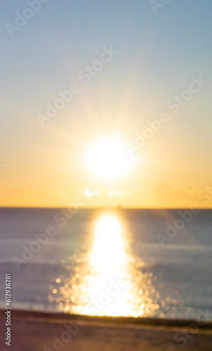 Blurred background. Sun shining in blue sky during sunset dawn. Sunrise dawning sundown. Sunny path, sunny walkway on surface of sea waves. Sunlight Sunbeams Sea landscape Natural blurry bokeh texture