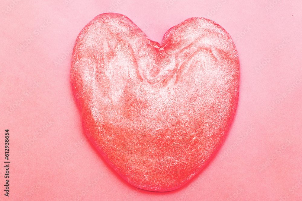 Red glitter slime in the form of a heart on pink background.
