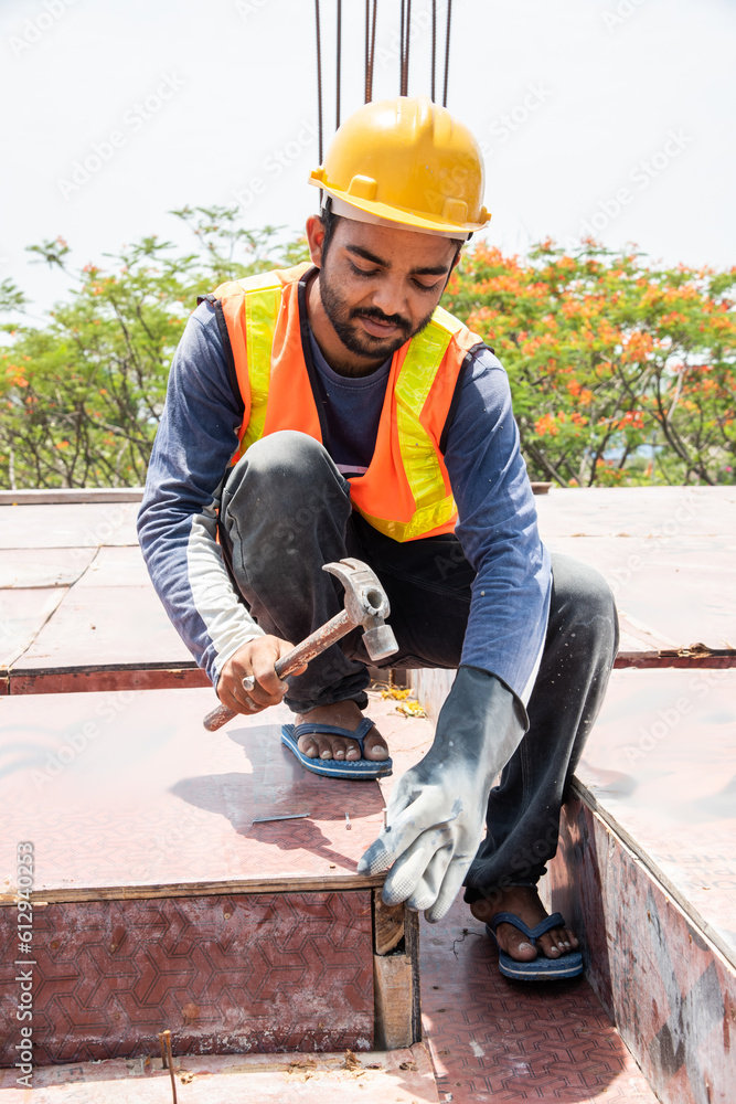 Indian asian male construction worker on site using nail with hammer preparing frame for slab Indian asian male construction worker on site using nail with hammer preparing frame for slab