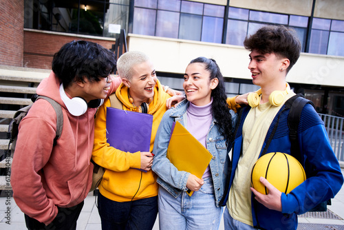 Group of gen z classmate and friends having fun outdoors high school. These cheerful students are two boys and two girls: four. Holding folders and a ball wile they hugging each other. © CarlosBarquero