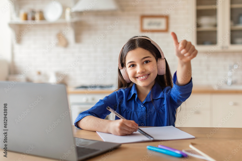 Schoolgirl At Laptop Learning And Gesturing Thumbs Up At Home Schoolgirl At Laptop Learning And Gesturing Thumbs Up At Home