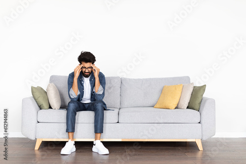 Unhappy middle eastern young man experiencing problems, living-room interior