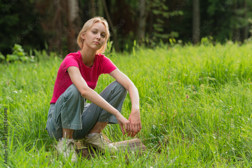 girl teenager squatting on a log in a meadow girl teenager squatting on a log in a meadow
