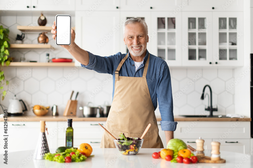 Dieting App. Smiling Senior Man Holding Blank Smartphone In Kitchen At Home Dieting App. Smiling Senior Man Holding Blank Smartphone In Kitchen At Home