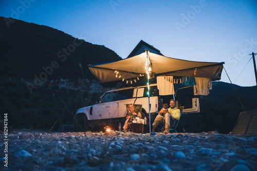 Man and woman with dogs camping in front of a 4x4 Offroad vehicle with roof tent at night time and romantic lighting on the beach
