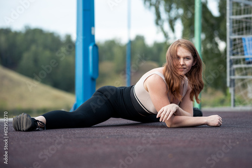 red-haired girl sits on the twine outdoors on the background of the sports ground