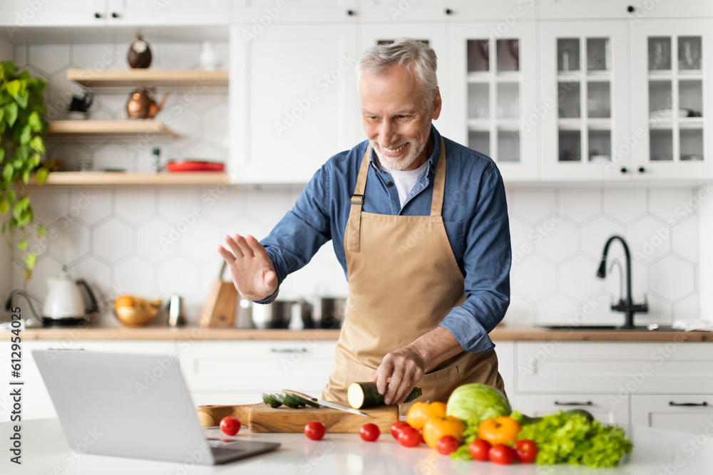 Online Cooking Class. Senior Man Using Laptop While Preparing Food In Kitchen Online Cooking Class. Senior Man Using Laptop While Preparing Food In Kitchen