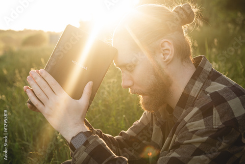 Fotografia Man praying on the holy Bible in a field during sunset, male sitting with closed eyes, concept for faith, spirituality, and religion