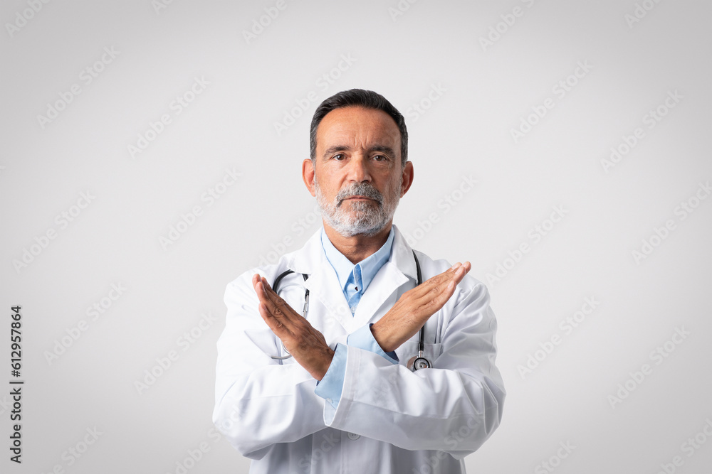 Sad serious confident caucasian mature man doctor in white coat crossed his arms, make stop gesture Sad serious confident caucasian mature man doctor in white coat crossed his arms, make stop gesture